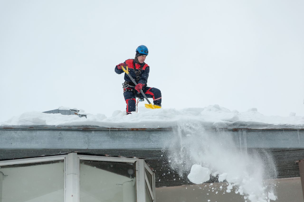 Alpinista wykonuje odśnieżanie dachu